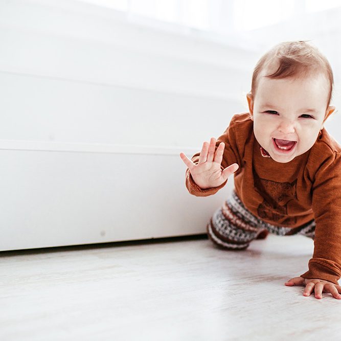 Happy child in orange sweater plays with feather on the floor